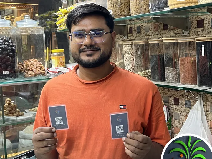 Mr. Arsalan of Madni Delight holding two TapStar All-in-One business cards in his dry fruits shop